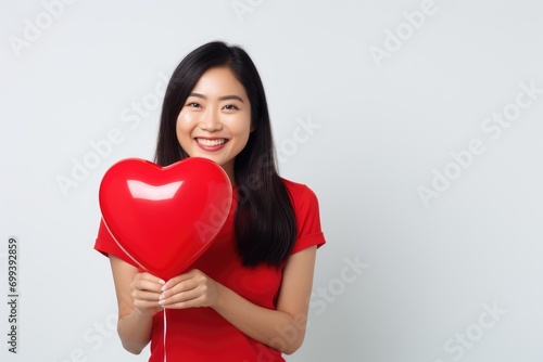 A woman holding a red heart shaped balloon