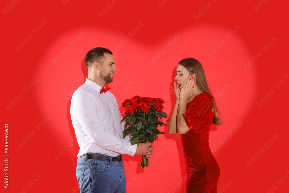 Young man giving bouquet of roses to his girlfriend with heart-shaped shadow on red background. Valentine's Day celebration Young man giving bouquet of roses to his girlfriend with heart-shaped shadow on red background. Valentine's Day celebration