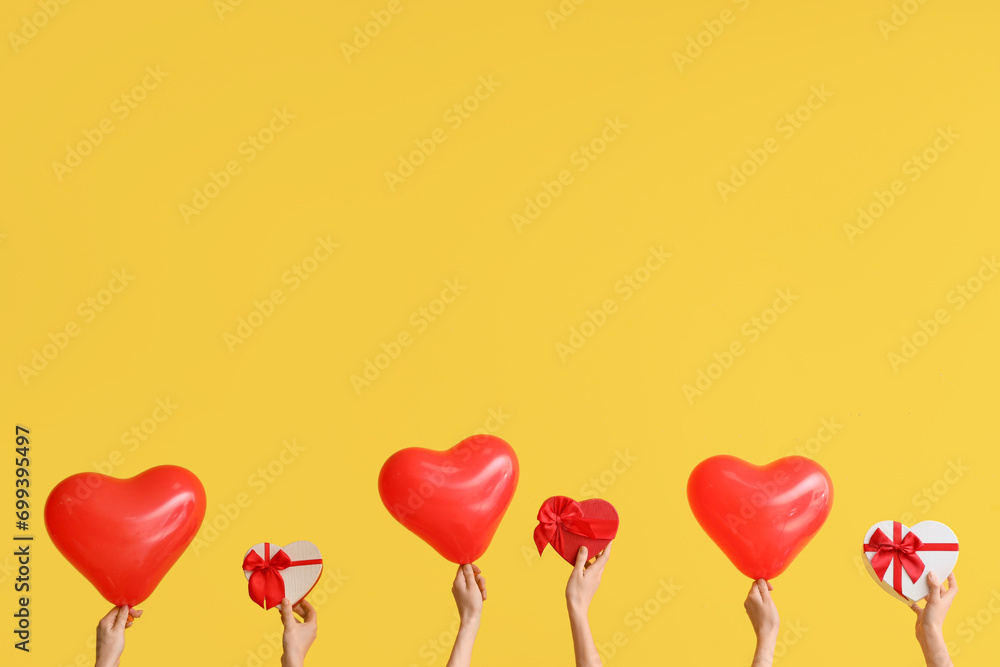 Female hands with gift boxes and heart shaped air balloons on yellow background. Valentine's Day celebration