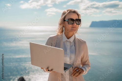 Freelance women sea. She is working on the computer. Good looking middle aged woman typing on a laptop keyboard outdoors with a beautiful sea view. The concept of remote work. © svetograph