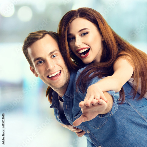 Sales, discounts, rebates, consumer credit concept - happy excited couple, in piggyback pose. Cheerful man and woman over blurred modern interior or mall background. photo