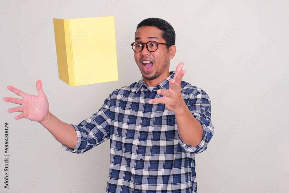 Adult Asian man showing wow expression when catching a book that falling from above Adult Asian man showing wow expression when catching a book that falling from above