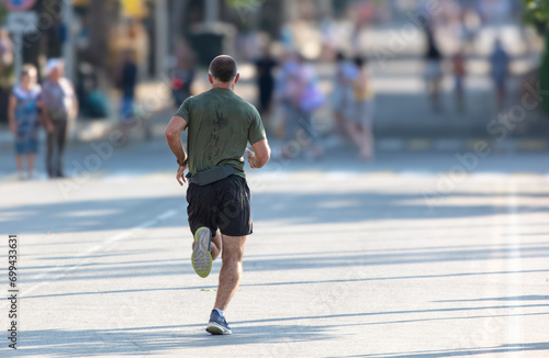 A man in shorts runs along the road in the city. Sport