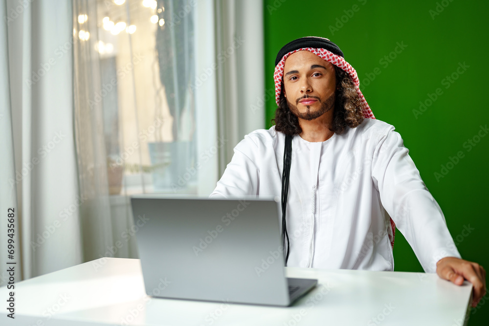 Young Arab man in traditional dress thobe working on computer in office Young Arab man in traditional dress thobe working on computer in office
