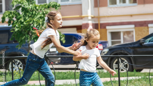 Girls play and run a race on the lawn outdoor street at the playground. Children's outdoor games. © Mariia