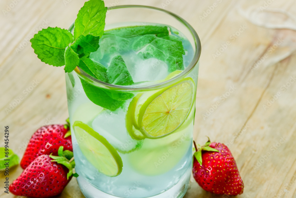 cold drink. in a transparent glass with water and ice there are slices of green lime and strawberries next to them cold drink. in a transparent glass with water and ice there are slices of green lime and strawberries next to them