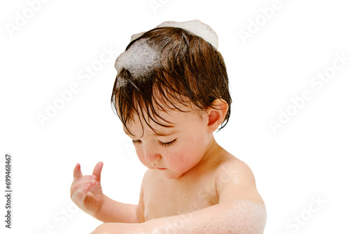 A happy child is playing with toys while sitting in a white homemade bathtub  isolated on white background. Little toddler baby boy bathes in a bubble bath. Kid aged one year six months