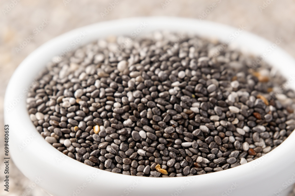 chia seeds. There is a white small plate with a lot of chia seeds on a light table, a health concept chia seeds. There is a white small plate with a lot of chia seeds on a light table, a health concept