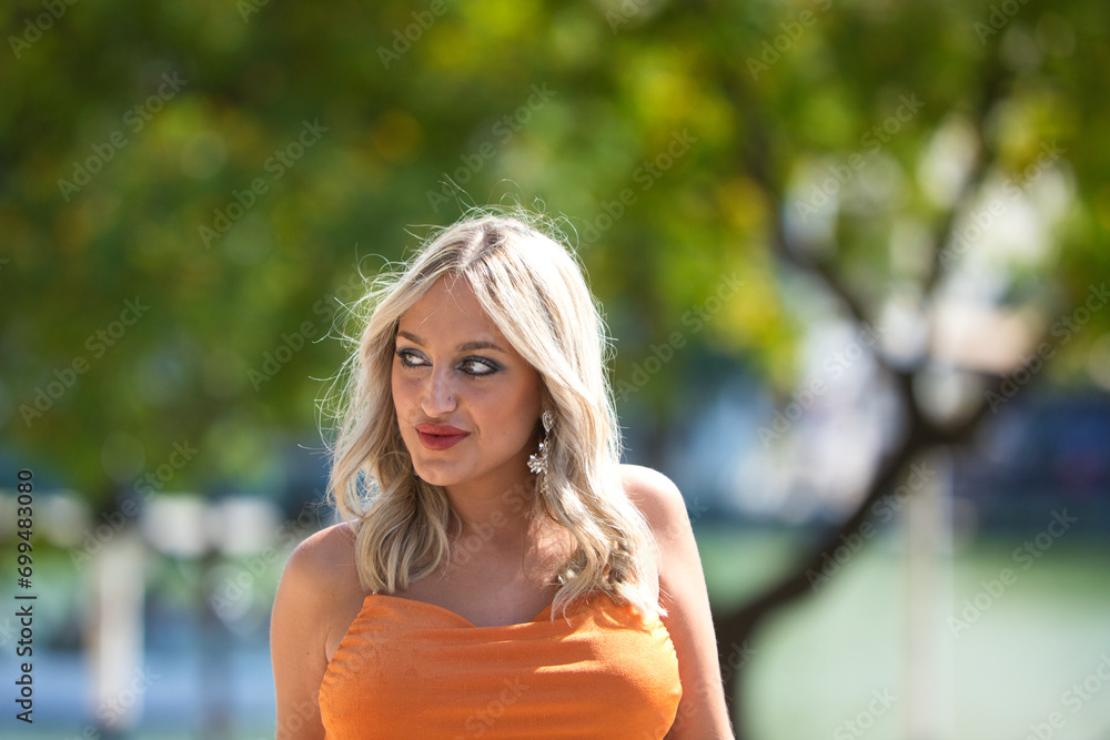 Beautiful young woman posing against cityscape in bright orange dress. Female tourist in bright dress enjoys city views on sunny days. Concept of lifestyle, fashion, travel. Beautiful young woman posing against cityscape in bright orange dress. Female tourist in bright dress enjoys city views on sunny days. Concept of lifestyle, fashion, travel.