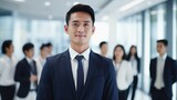 Portrait of a handsome smiling asian businessman boss in a suit standing in his modern business company office. his workers standing in the blurry background