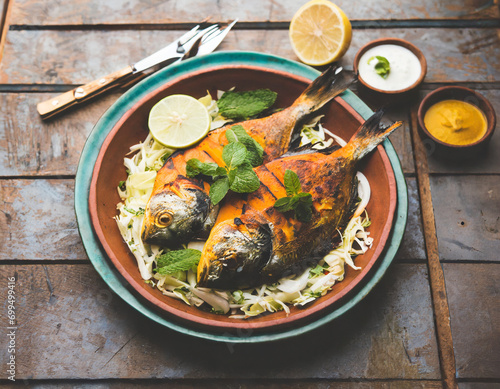 Tandoori Pomfret fish cooked in a clay oven and garnished with lemon , mint, cabbage and carrot salad photo