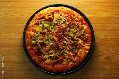 Pizza with meat and vegetables in a black plate on a wooden table