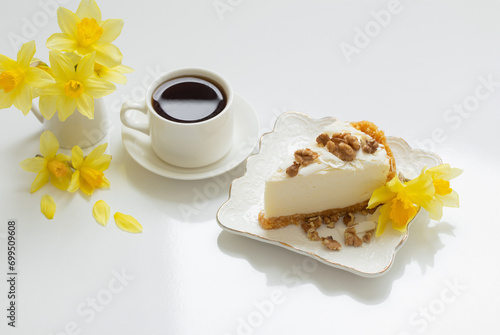 cheesecake with cup of coffee and yellow spring flowers on white table