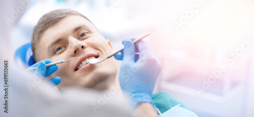 Happy young men getting dental checkup at dentistry clinic  banner with sunlight. Dentist using equipment for examination of teeth of man patient