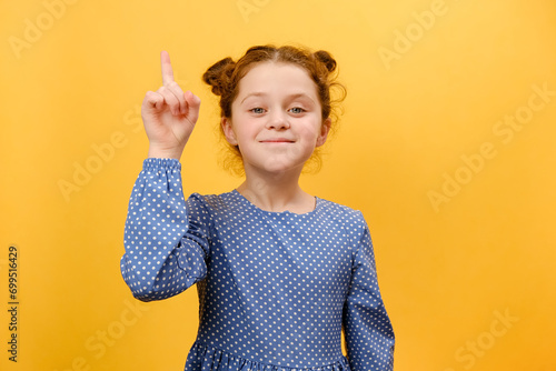 Portrait of inspired preteen girl child with open mouth pointing finger up in inspiration, having solution for problem, posing isolated over plain yellow color background wall in studio. Idea concept photo