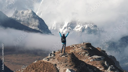 Tourist explorer with backpack hiking in mountains of Himalayas. At top of mountain he raises arms up celebrating achievements and success of ascent. Trekking through Nepal to Everest Base Camp photo