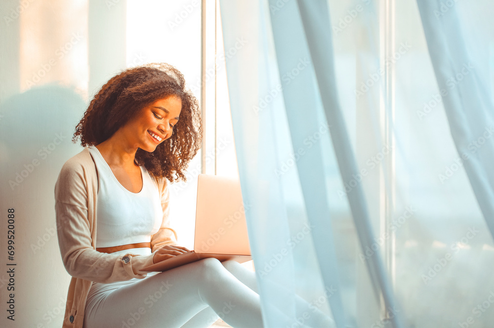 Happy african american young woman freelancer on windowsill with laptop on laps, working from home Happy african american young woman freelancer on windowsill with laptop on laps, working from home