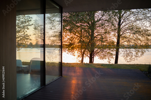Serene Sunset View Through Large Window of Modern Home Overlooking a Lake with Trees Bathed in Golden Light