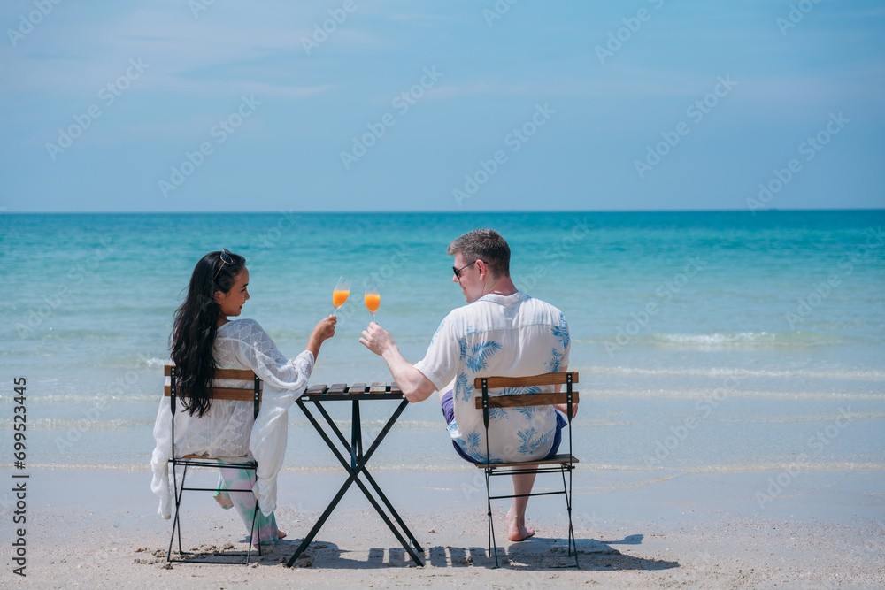 Obraz premium Happy and loving young couple drink orange juice at tropical beach. Couple Enjoying Fun and Romance by the Ocean.