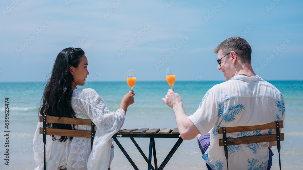 Obraz premium Happy and loving young couple drink orange juice at tropical beach. Couple Enjoying Fun and Romance by the Ocean.