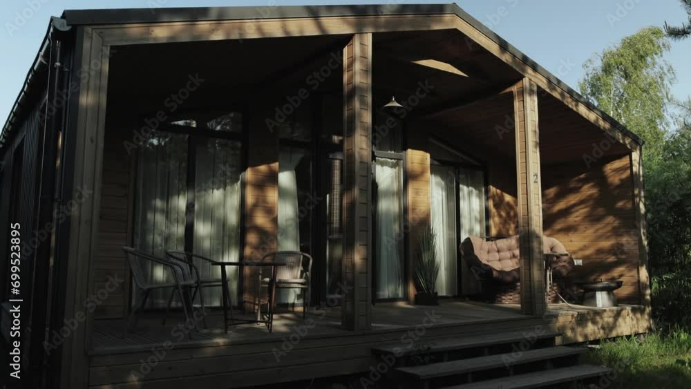 Cozy terrace in the wooden tiny house. Terrace in a small country house in the forest at summer. Table and brown sofa, shadows from trees on the wooden wall, slow motion. Cozy terrace in the wooden tiny house. Terrace in a small country house in the forest at summer. Table and brown sofa, shadows from trees on the wooden wall, slow motion.