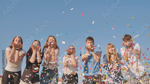 Friends blow colorful paper confetti on a sunny day.