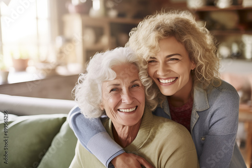 Joyful senior Caucasian mother and curly-haired daughter embracing, sharing genuine smiles in a cozy home environment. photo
