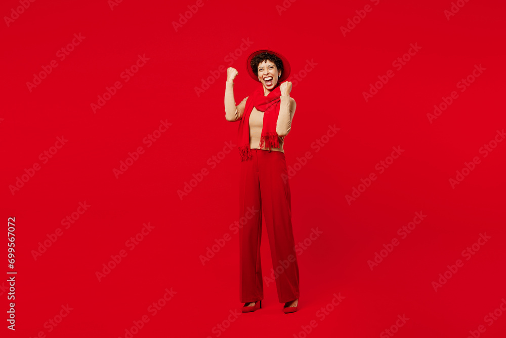 Full body overjoyed excited happy young woman of African American ethnicity she wearing beige sweater hat scarf do winner gesture isolated on plain red background studio portrait. Lifestyle concept. Full body overjoyed excited happy young woman of African American ethnicity she wearing beige sweater hat scarf do winner gesture isolated on plain red background studio portrait. Lifestyle concept.