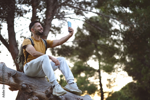 hiker taking a selfie with his smartphone sitting on a tree trunk photo
