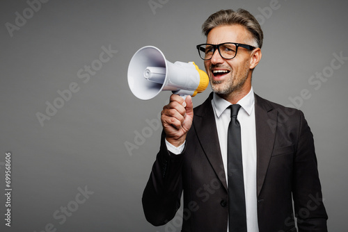 Adult employee business man corporate lawyer in classic black suit shirt tie work in office hold megaphone scream announce discounts sale look aside isolated on plain grey background studio portrait