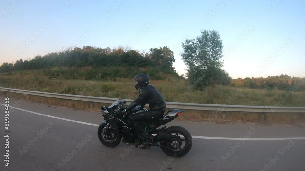 Motorcyclist racing his motorcycle on country road. Guy driving bike during trip. Young man in helmet riding fast on modern sport motorbike at highway. Side view Close up Slow motion Motorcyclist racing his motorcycle on country road. Guy driving bike during trip. Young man in helmet riding fast on modern sport motorbike at highway. Side view Close up Slow motion
