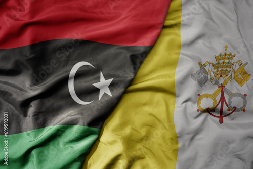 big waving national colorful flag of vatican city and national flag of libya .