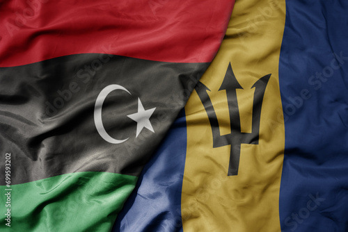 big waving national colorful flag of barbados and national flag of libya .