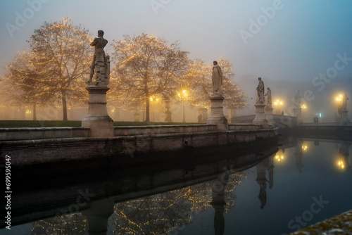 Padua, Italy - December 14, 2023: Prato della Valle, statues and trees with Christmas lights immersed in fog.