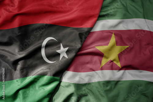 big waving national colorful flag of suriname and national flag of libya .