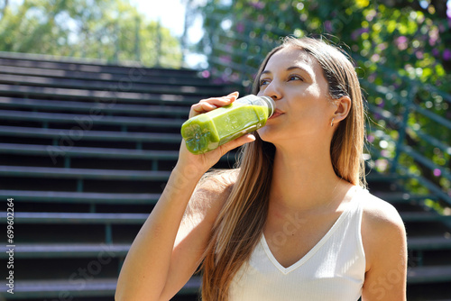 Beautiful healthy young woman drinking green smoothie detox juice outdoors