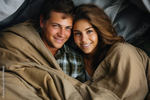 Young couple lying under blanket in bedroom, top view