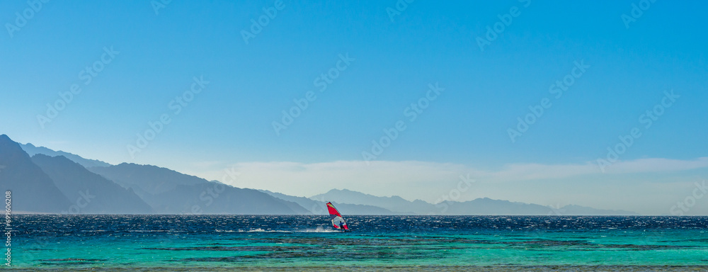 surfer rides in the Red Sea against the backdrop of high rocky mountains and a blue sky with clouds in Egypt Dahab