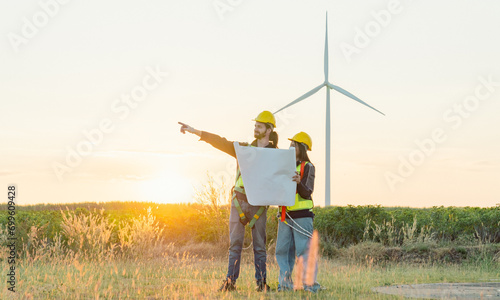 Caucasian engineer man and female engineering worker builders are looking for wind turbine blueprint drawings for wind turbine construction at a windmill field farm.