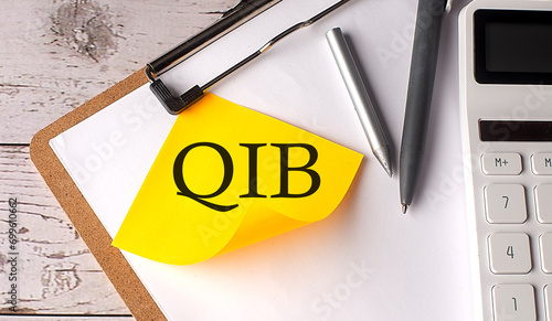 QIB word on a yellow sticky with calculator, pen and clipboard photo
