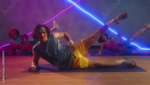 Male coach and two biracial sportswomen doing side leg raises on floor in retro outfits photo
