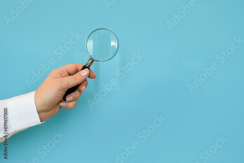 A hand in a white shirt holds a magnifying glass on a blue background with a copy space