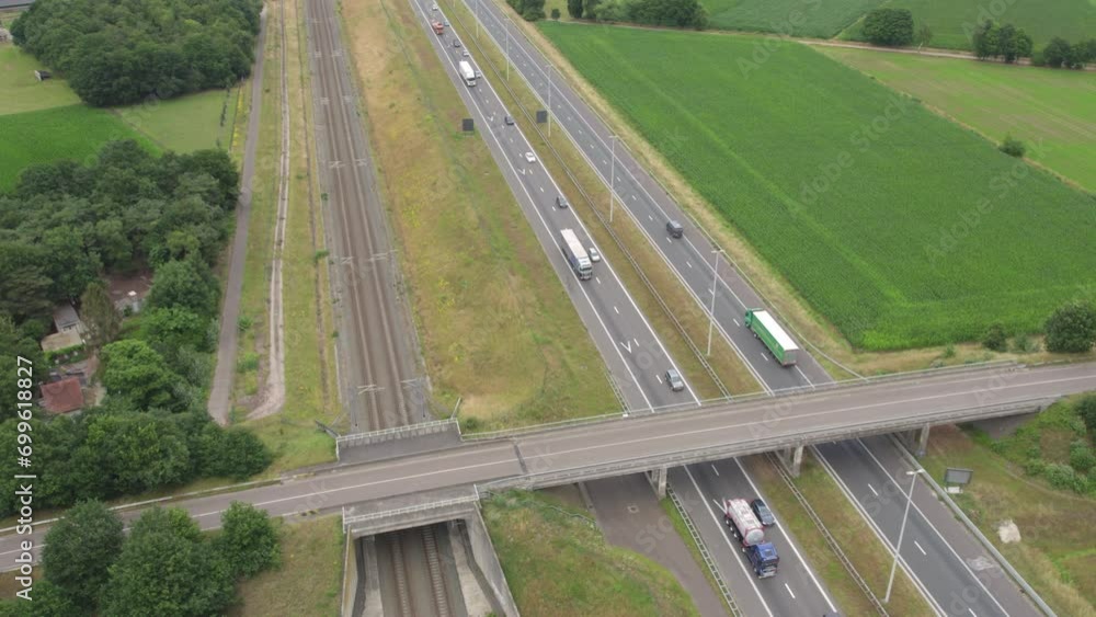 This drone footage captures the bustling activity of a highway as it cuts through the calm of the surrounding countryside. The contrast between the steady flow of traffic and the tranquil green fields