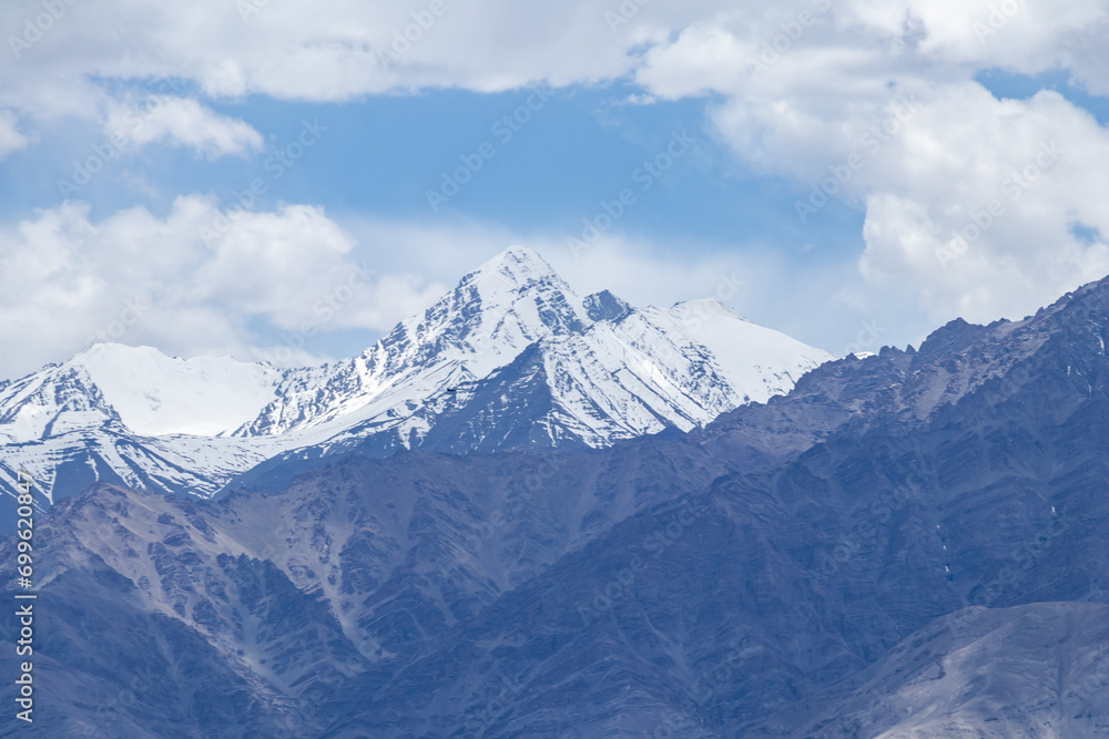 A hazy shot of snow-capped Himalaya peaks with cloudy blue sky.