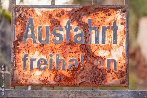 old rusty sign Ausfahrt freihalten, english keep way, at an old gate