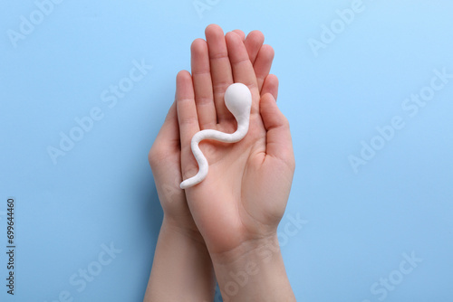 Reproductive medicine. Woman holding figure of sperm cell on light blue background, top view photo