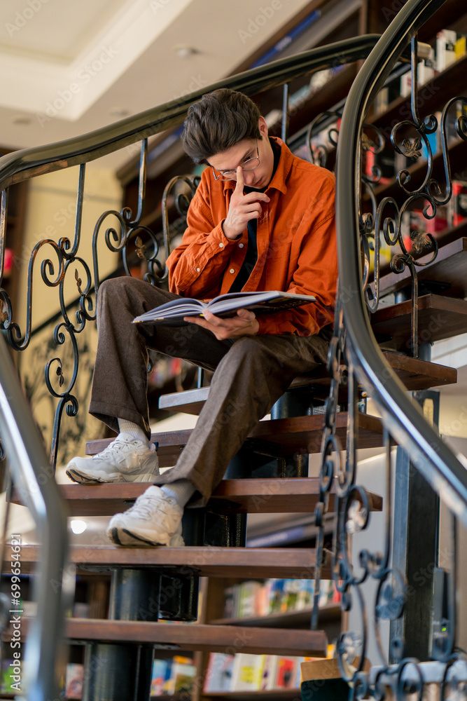a young guy in glasses sits on the stairs carefully reads a book a manual prepares for exams