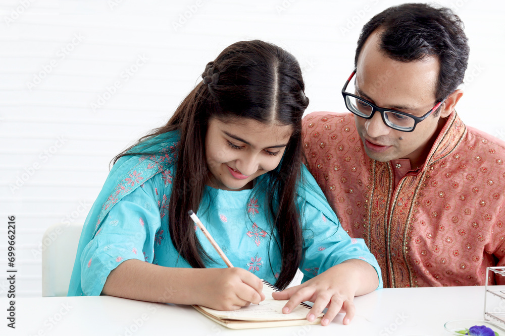 Cute Indian school student girl in India traditional dress doing homework with her father. Dad teaching daughter kid at home, parent become teacher tutor involvement in childhood education in family. Cute Indian school student girl in India traditional dress doing homework with her father. Dad teaching daughter kid at home, parent become teacher tutor involvement in childhood education in family.