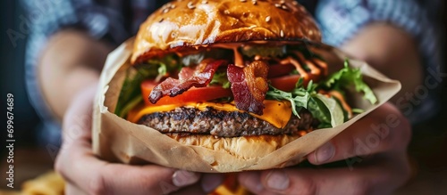 Man's hands holding a hamburger with bacon, salad, and cheese on a menu banner.