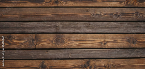 This image shows a close-up view of a wooden surface, characterized by horizontal planks with visible grains and textures. The wood has a dark brown color, and the lines between the planks are clearly